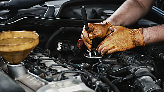 En mekaniker med handsker arbejder på en bilmotor under en åben motorhjelm