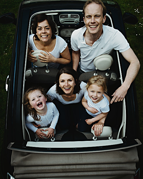 En familie med tre børn sidder smilende sammen i en åben bil